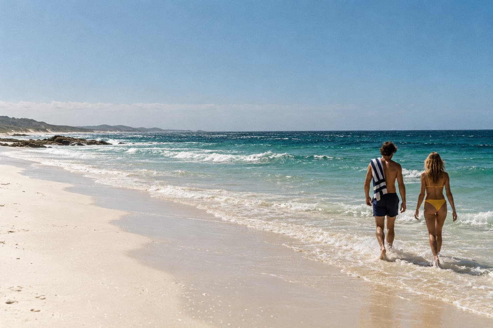 Two swimmers walking into a wide Australian beach at midday